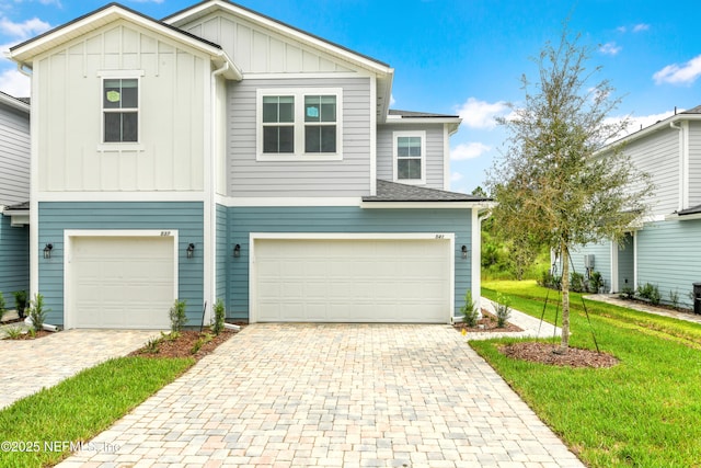 view of front of property with decorative driveway, a shingled roof, board and batten siding, a garage, and a front lawn