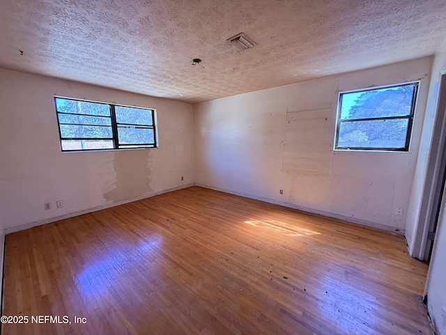 unfurnished room featuring a textured ceiling, baseboards, visible vents, and light wood-style floors