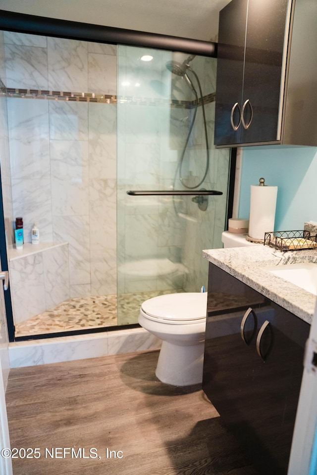 bathroom with toilet, a tile shower, wood finished floors, and vanity