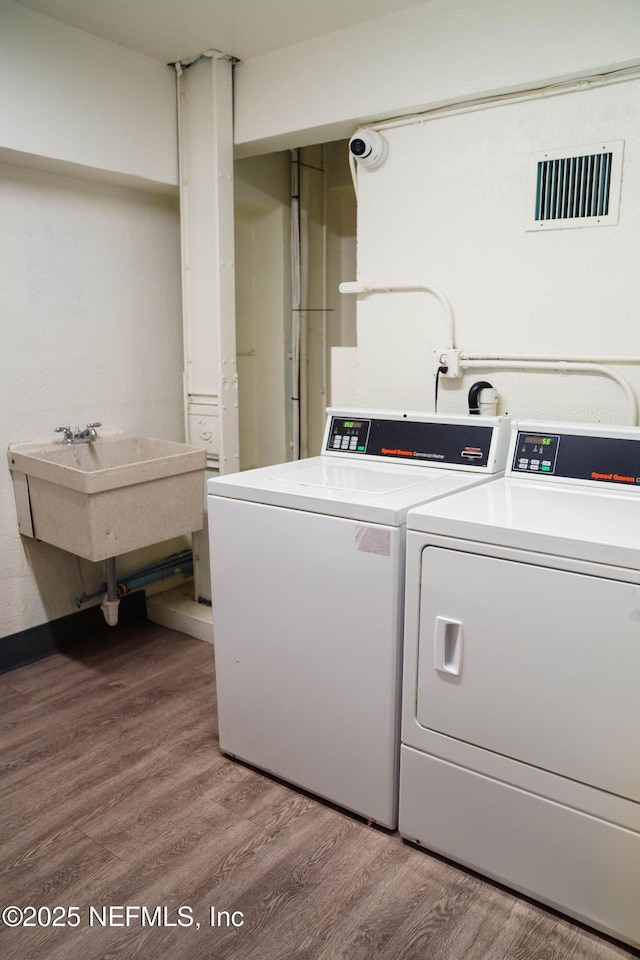 shared laundry area featuring visible vents, a sink, washer and clothes dryer, and wood finished floors