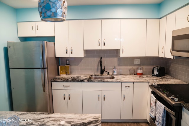 kitchen with tasteful backsplash, white cabinets, light stone countertops, stainless steel appliances, and a sink