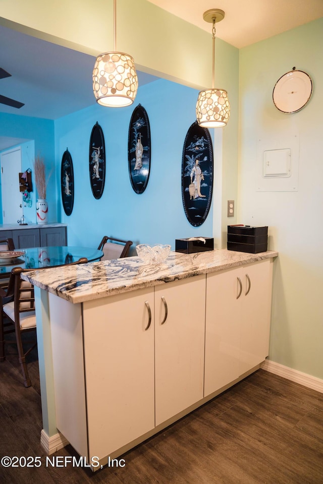 kitchen with light stone counters, decorative light fixtures, dark wood-type flooring, white cabinetry, and baseboards