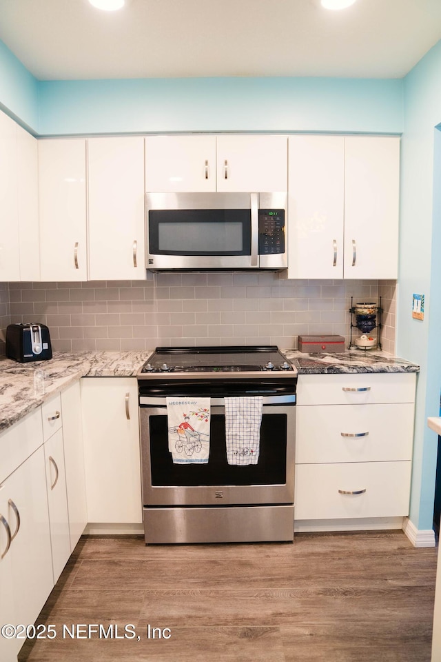 kitchen featuring appliances with stainless steel finishes, white cabinetry, light wood-style floors, and tasteful backsplash