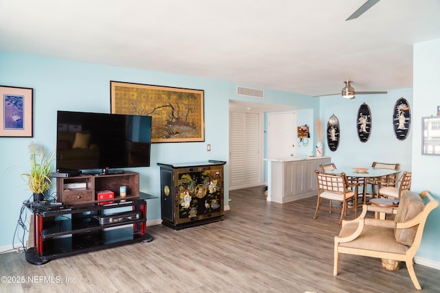 living area featuring a ceiling fan, visible vents, baseboards, and wood finished floors