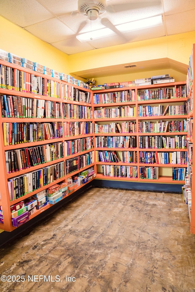 living area featuring bookshelves, a paneled ceiling, and a ceiling fan