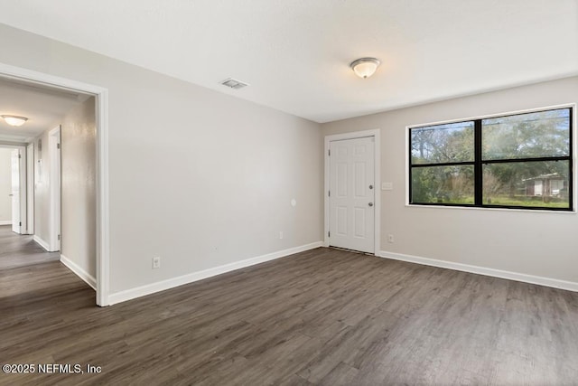 spare room featuring dark wood-style floors, visible vents, and baseboards