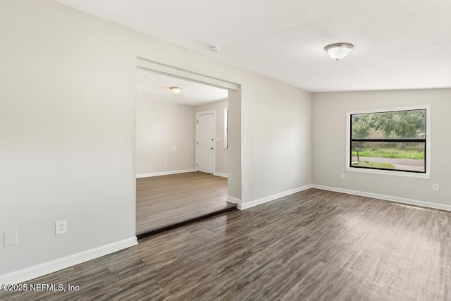 spare room featuring baseboards and dark wood-type flooring