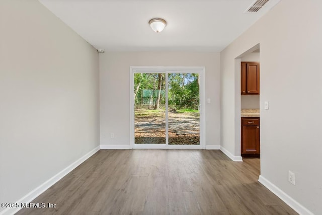 empty room with wood finished floors, visible vents, and baseboards