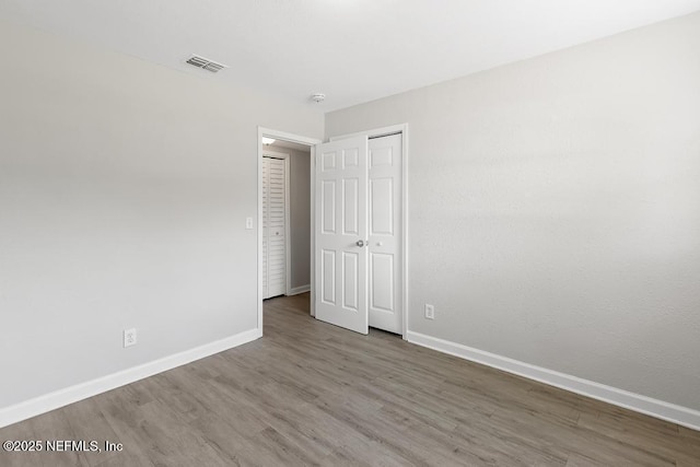 unfurnished bedroom featuring a closet, visible vents, baseboards, and wood finished floors