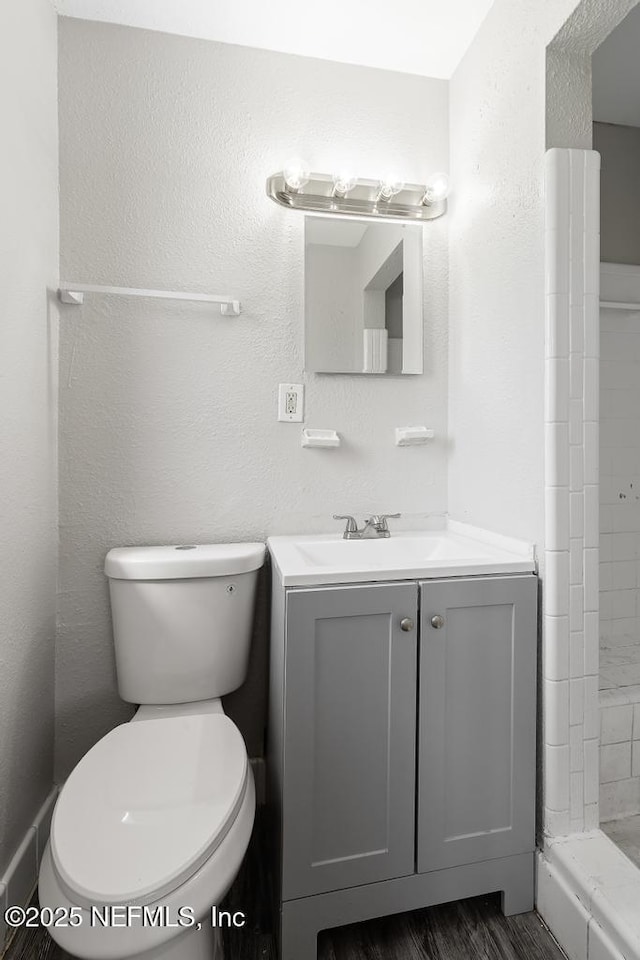 full bath featuring a textured wall, toilet, a tile shower, vanity, and wood finished floors