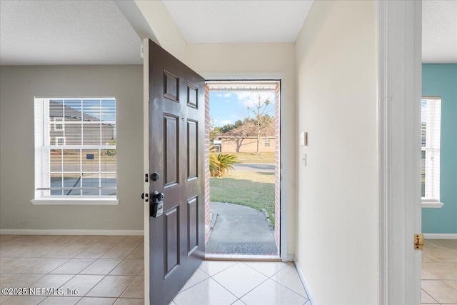 foyer entrance with light tile patterned floors, a textured ceiling, a wealth of natural light, and baseboards