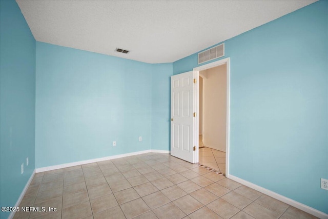 empty room featuring visible vents, a textured ceiling, baseboards, and light tile patterned floors