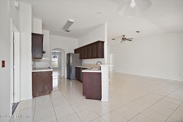 kitchen with arched walkways, light tile patterned floors, light countertops, freestanding refrigerator, and open floor plan