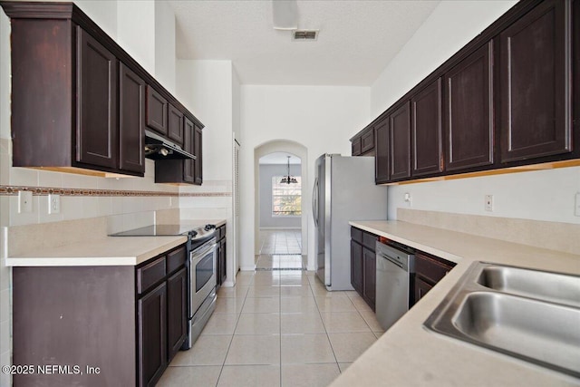 kitchen with arched walkways, light countertops, appliances with stainless steel finishes, and under cabinet range hood