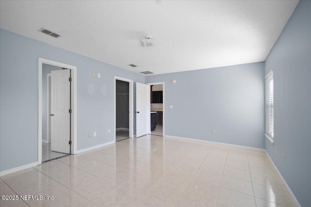 spare room featuring a textured ceiling, light tile patterned flooring, visible vents, and baseboards