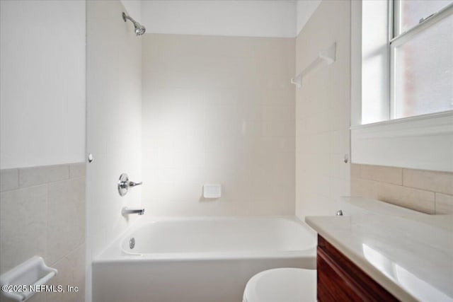 bathroom with toilet, shower / bathing tub combination, tile walls, and vanity