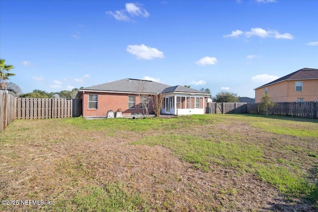 back of property featuring a sunroom, brick siding, a yard, and a fenced backyard