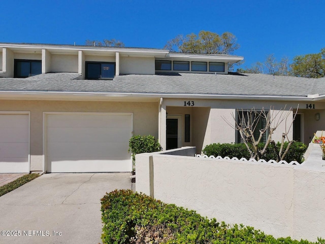 townhome / multi-family property with a garage, concrete driveway, roof with shingles, and stucco siding