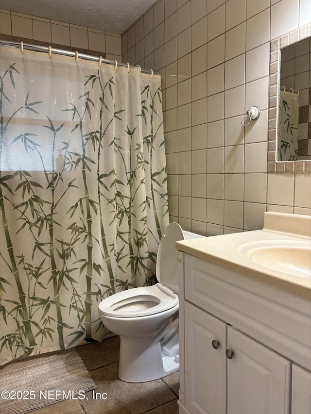 bathroom with tile walls, toilet, a shower with shower curtain, vanity, and a textured ceiling