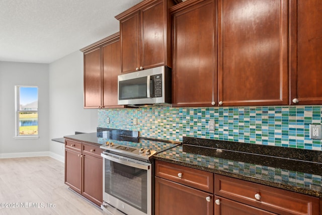 kitchen with dark stone countertops, stainless steel appliances, baseboards, and backsplash