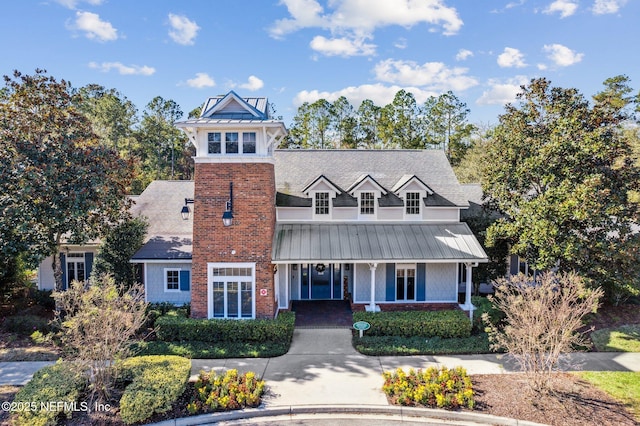 view of front of house featuring a standing seam roof, a porch, brick siding, and metal roof