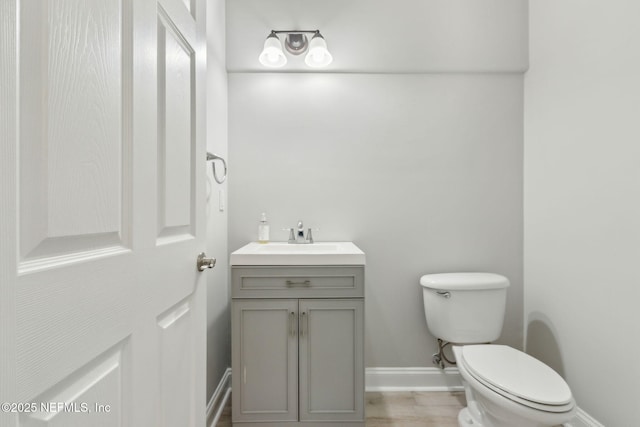 half bathroom with vanity, toilet, wood finished floors, and baseboards