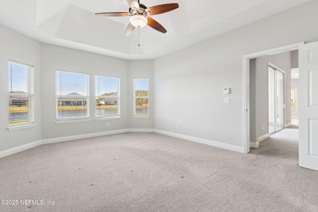 carpeted empty room with ceiling fan, a raised ceiling, and baseboards