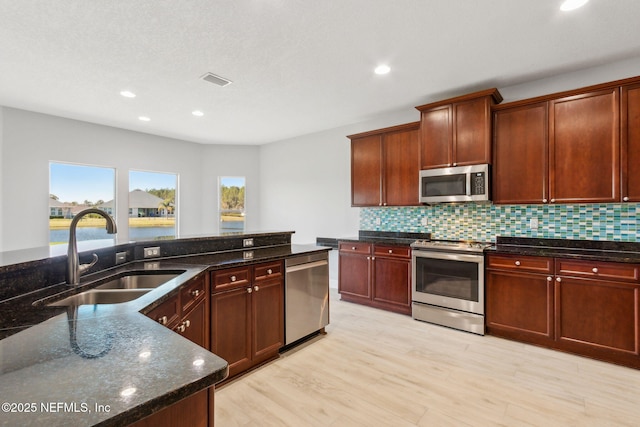 kitchen with a sink, dark stone countertops, decorative backsplash, and stainless steel appliances