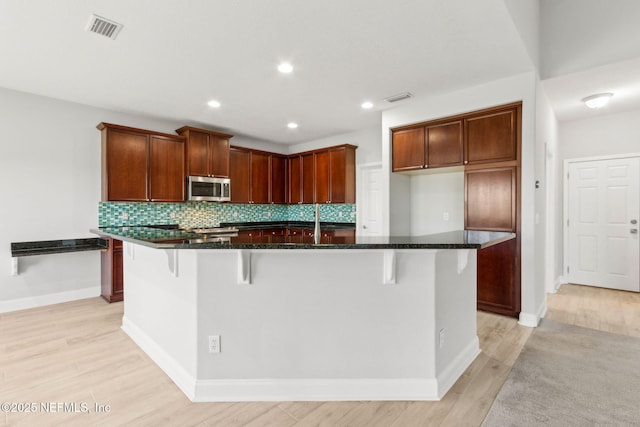 kitchen featuring stainless steel microwave, dark stone countertops, visible vents, and decorative backsplash