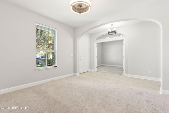 carpeted empty room featuring arched walkways and baseboards