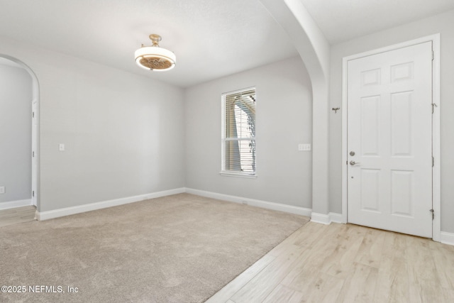 entryway with baseboards, arched walkways, and light carpet