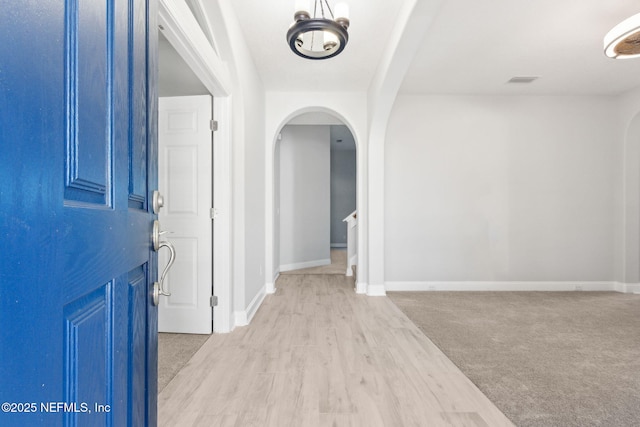 foyer featuring arched walkways, light colored carpet, light wood finished floors, and baseboards