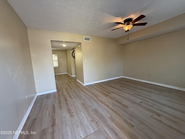 unfurnished room with a textured ceiling, ceiling fan, wood finished floors, visible vents, and baseboards