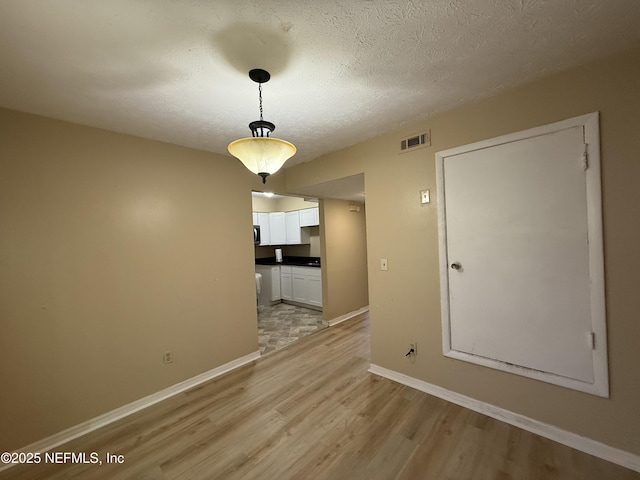 unfurnished dining area with light wood-type flooring, visible vents, a textured ceiling, and baseboards