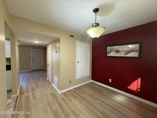 empty room with light wood-style floors, visible vents, and baseboards