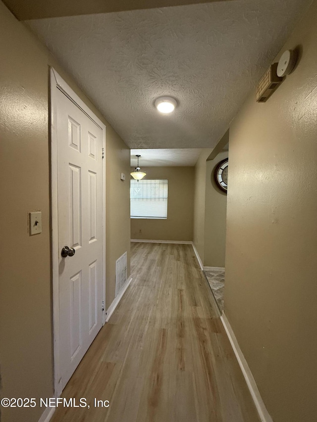 hallway featuring a textured ceiling, baseboards, visible vents, and light wood-style floors