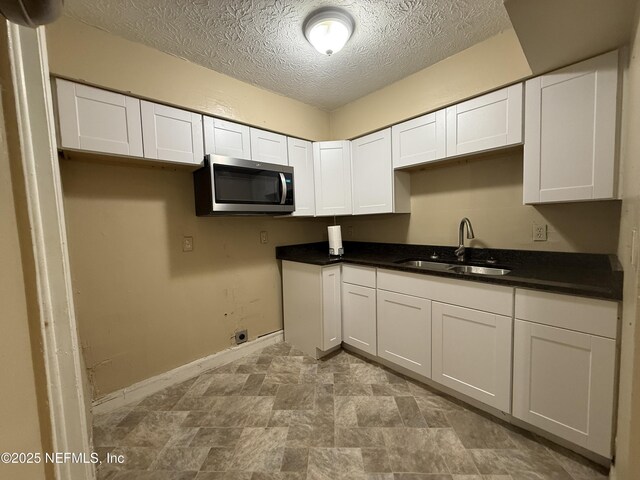 kitchen with dark countertops, stainless steel microwave, white cabinetry, a sink, and a textured ceiling