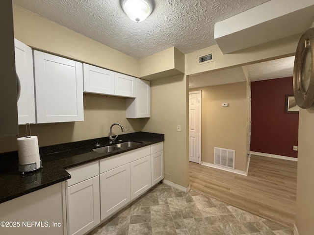 kitchen with a textured ceiling, a sink, visible vents, and white cabinets