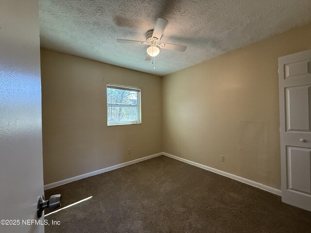 empty room featuring dark carpet, a textured ceiling, baseboards, and ceiling fan