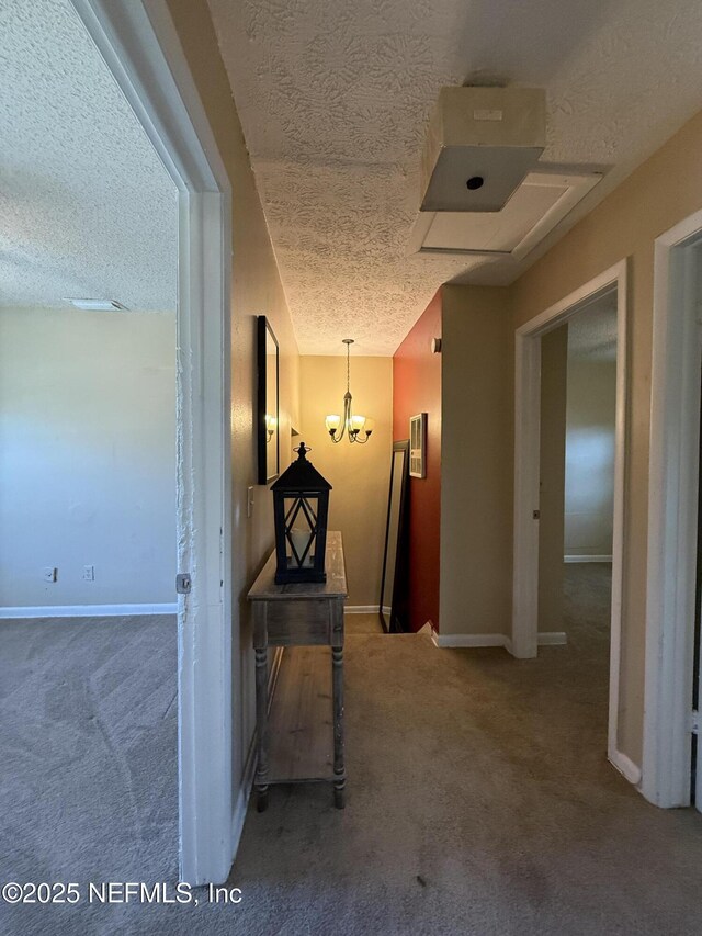 corridor with a textured ceiling, carpet, a chandelier, and baseboards