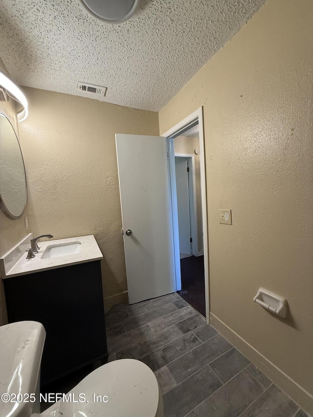 bathroom featuring wood finish floors, visible vents, a textured wall, vanity, and baseboards