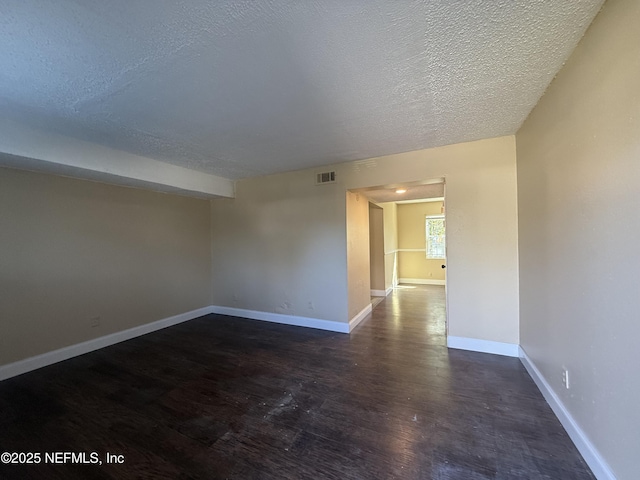 unfurnished room with visible vents, a textured ceiling, baseboards, and dark wood-style flooring