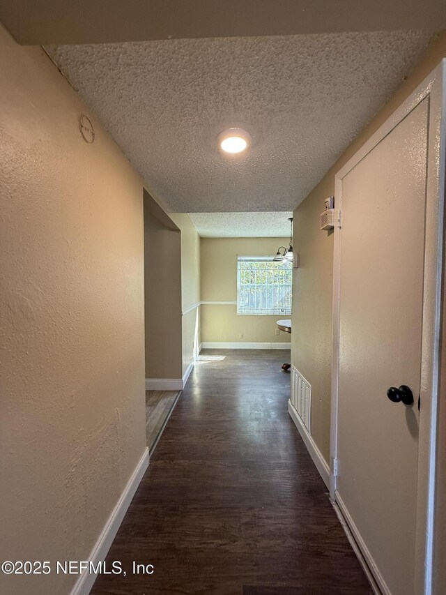 hallway featuring a textured ceiling, baseboards, wood finished floors, and a textured wall