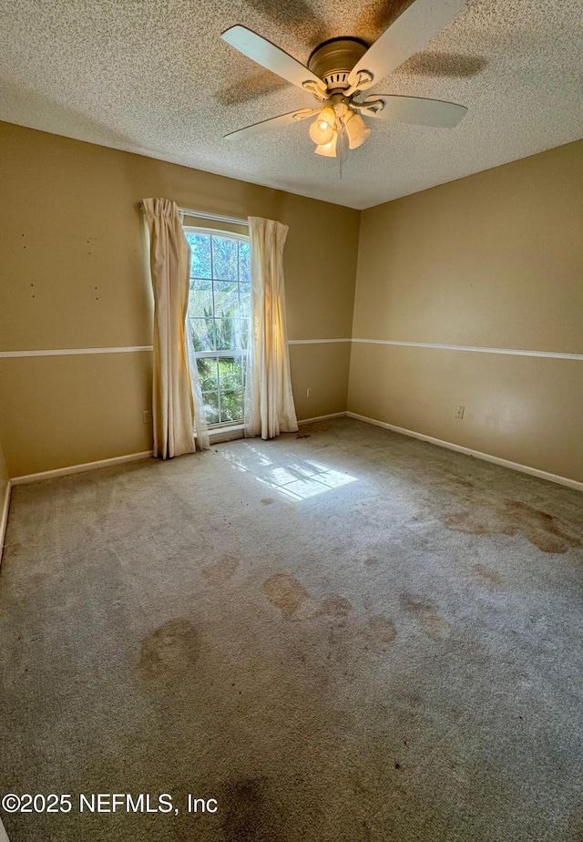 carpeted spare room featuring baseboards, a textured ceiling, and ceiling fan