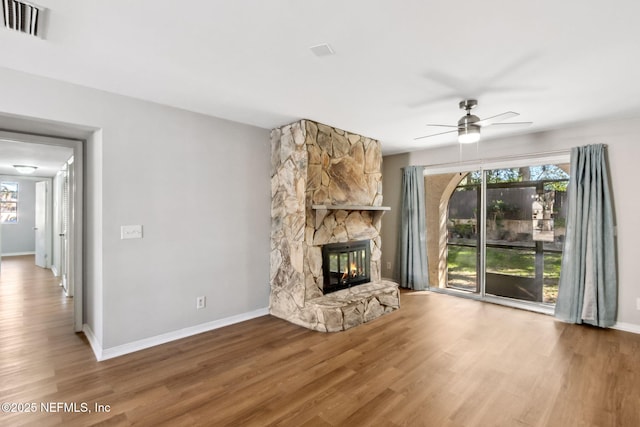 unfurnished living room featuring a stone fireplace, wood finished floors, and a healthy amount of sunlight