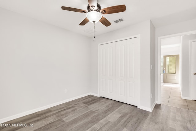 unfurnished bedroom featuring ceiling fan, wood finished floors, visible vents, baseboards, and a closet