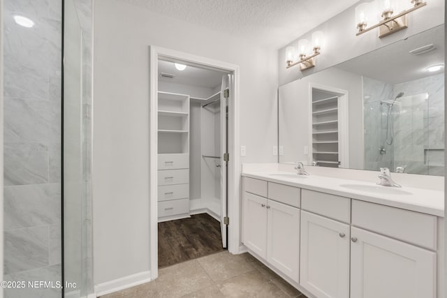 full bathroom with a stall shower, a sink, a textured ceiling, and a spacious closet