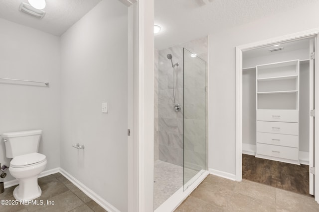 full bath with a textured ceiling, a shower stall, toilet, and baseboards