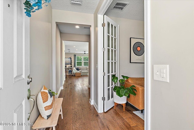 corridor with baseboards, visible vents, wood-type flooring, and a textured ceiling