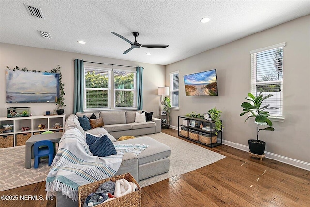 living area with a ceiling fan, wood finished floors, visible vents, and baseboards